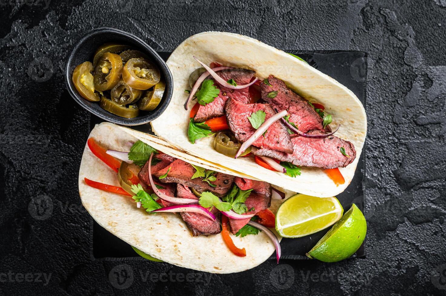 Mexican Steak Tacos with beef meat, cilantro, green sauce, jalapenos and onion. Black background. top view photo