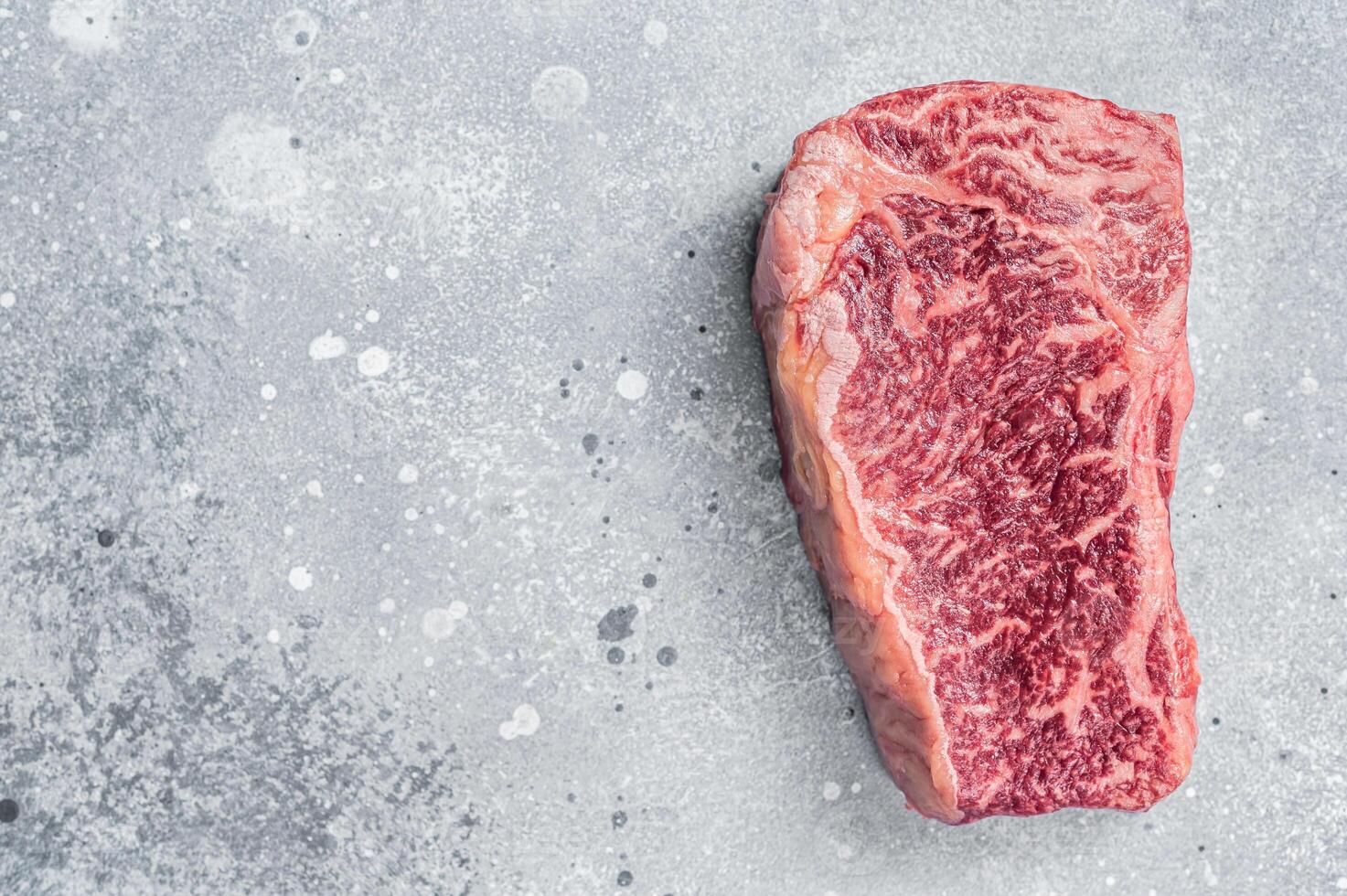Raw Wagyu striploin or New york steak on a butcher table. Gray background. Top view. Copy space photo