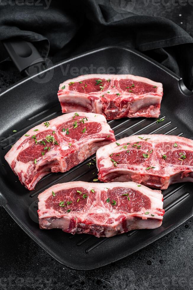 Raw lamb loin rib chops steaks in grill skillet with rosemary and thyme. Black background. Top view photo