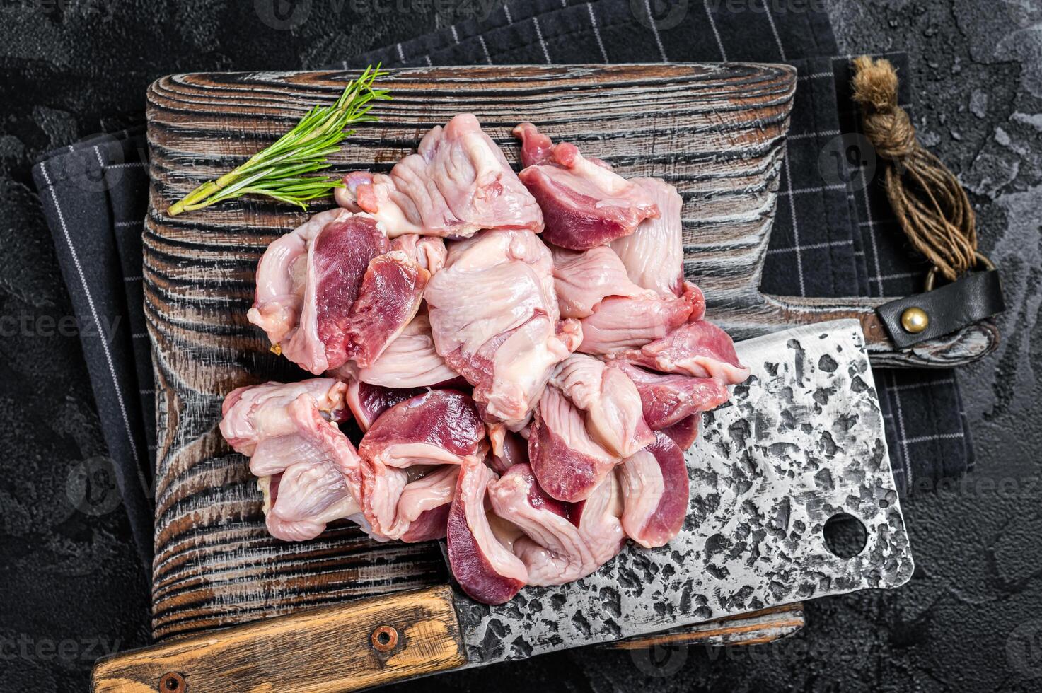 Raw chicken stomachs, giblets gizzards on a butcher board with meat cleaver. Black background. Top view photo