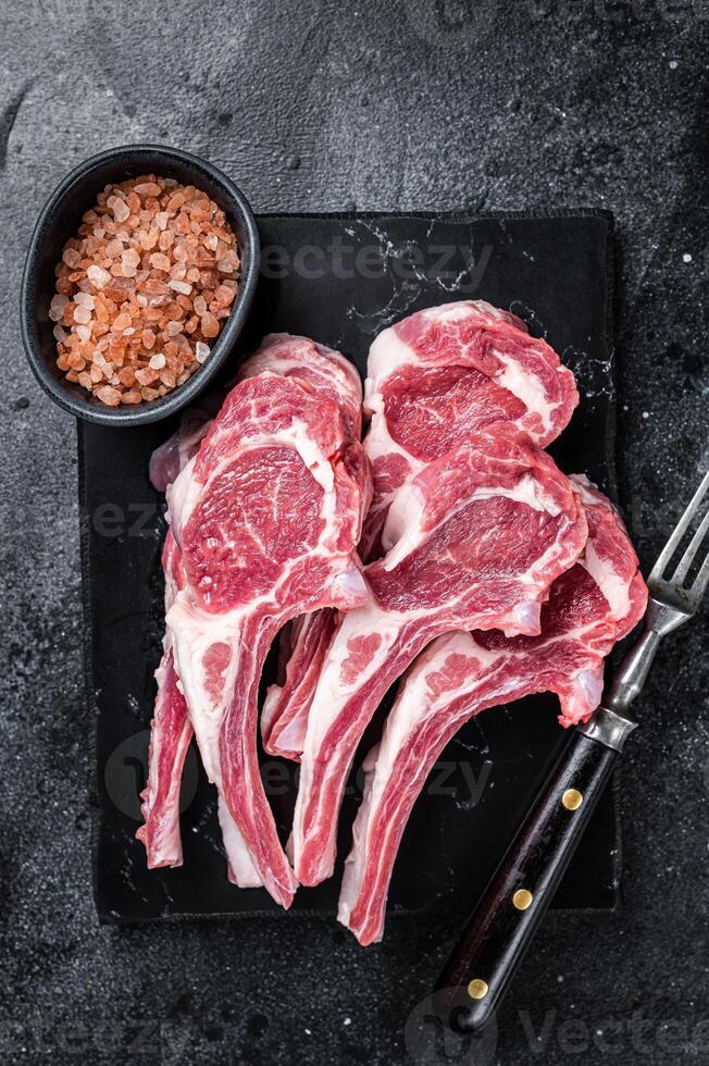 Uncooked lamb mutton chops, raw meat steaks. Black background. Top view photo