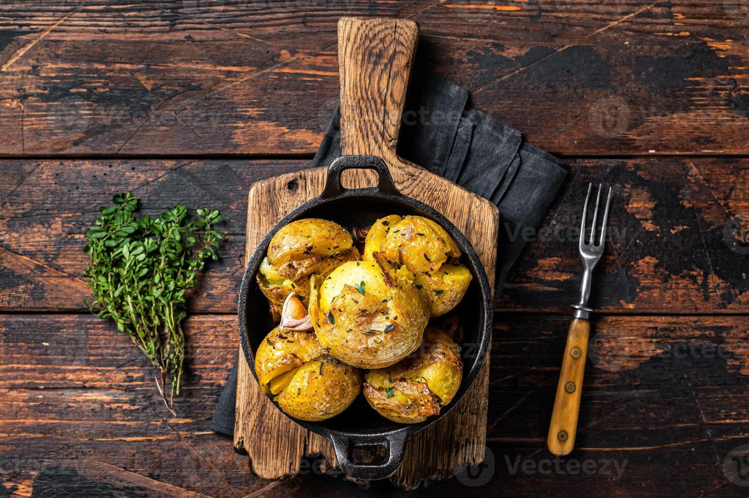 Crushed, Broken potatoes baked in oil with herbs. Wooden background. Top view photo