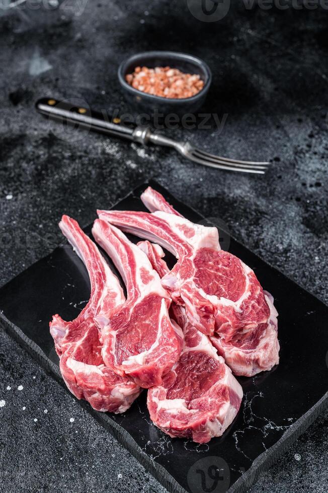Uncooked lamb mutton chops, raw meat steaks. Black background. Top view photo