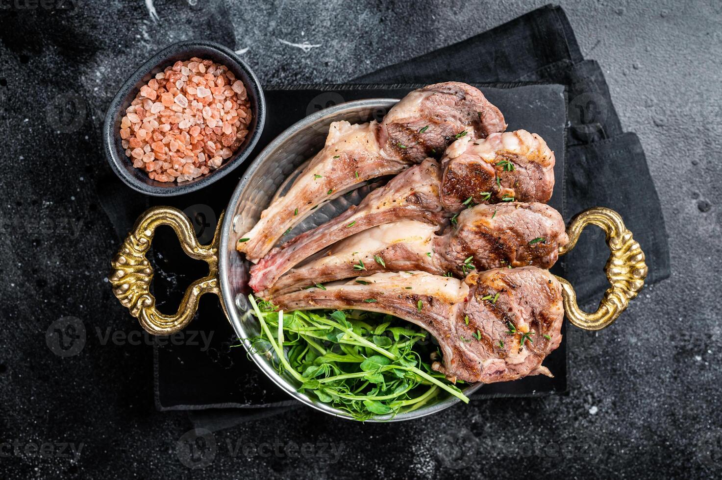 Grilled Lamb mutton Chops steaks in a skillet with green salad. Black background. Top view photo