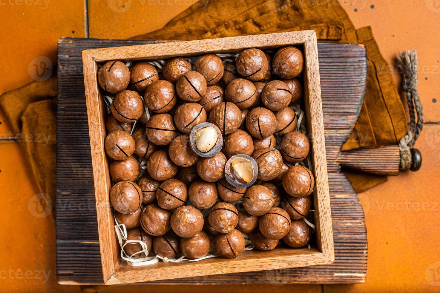 Macadamia natural nuts in a box. Orange background. Top view photo
