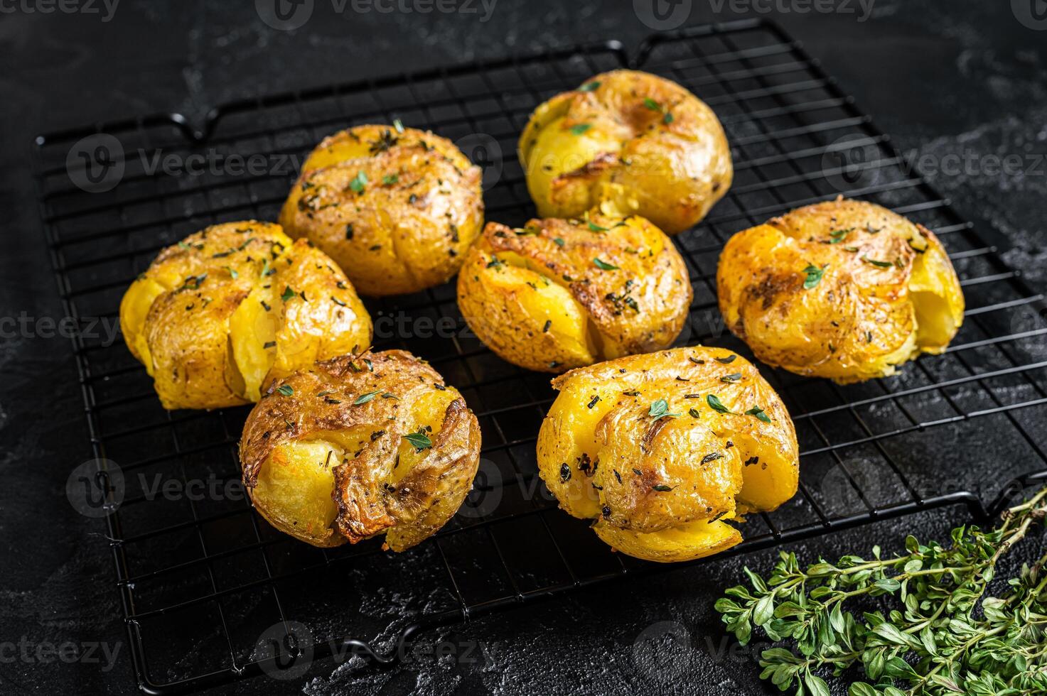 Crushed, smashed potatoes baked with rosemary and thyme. Black background. Top view photo