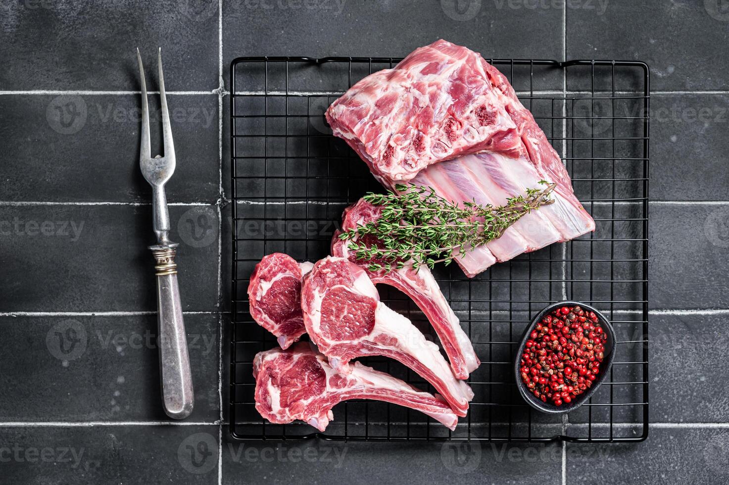 Fresh Raw lamb meat chop steaks on kitchen table with spices and herbs. Black background. Top view photo