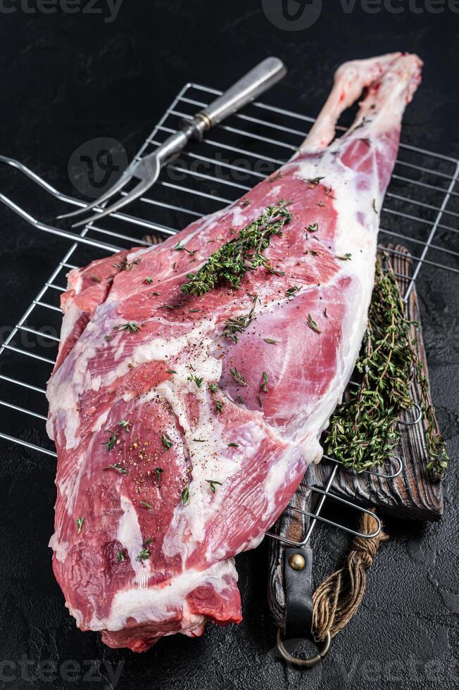 Marinated raw lamb mutton Leg Thigh with thyme and spices. Black background. Top view photo