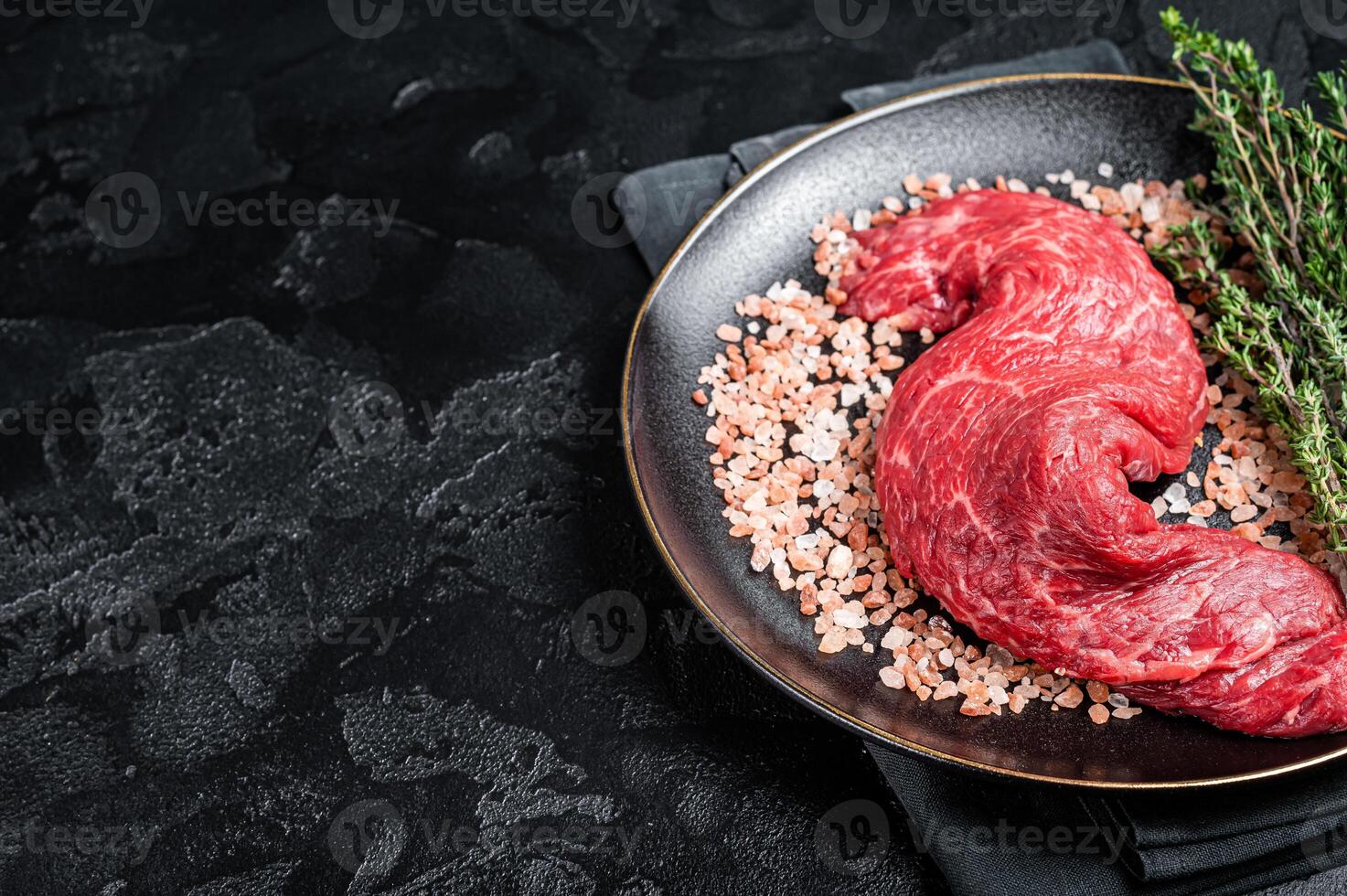 Raw Machete beef meat steak or hanging tender cut on plate with sea salt and thyme. Black background. Top view. Copy space photo