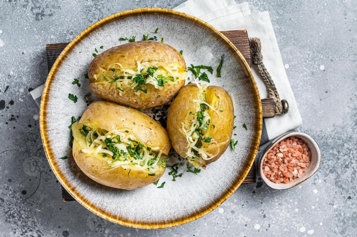 Baked Jacket potatoes with cheese and butter. Gray background. Top view photo