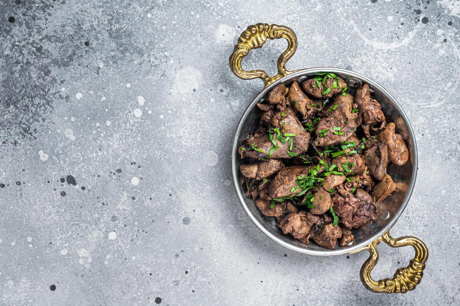 Chicken liver stew with onions and parsley in a skillet. Gray background. Top view. Copy space photo