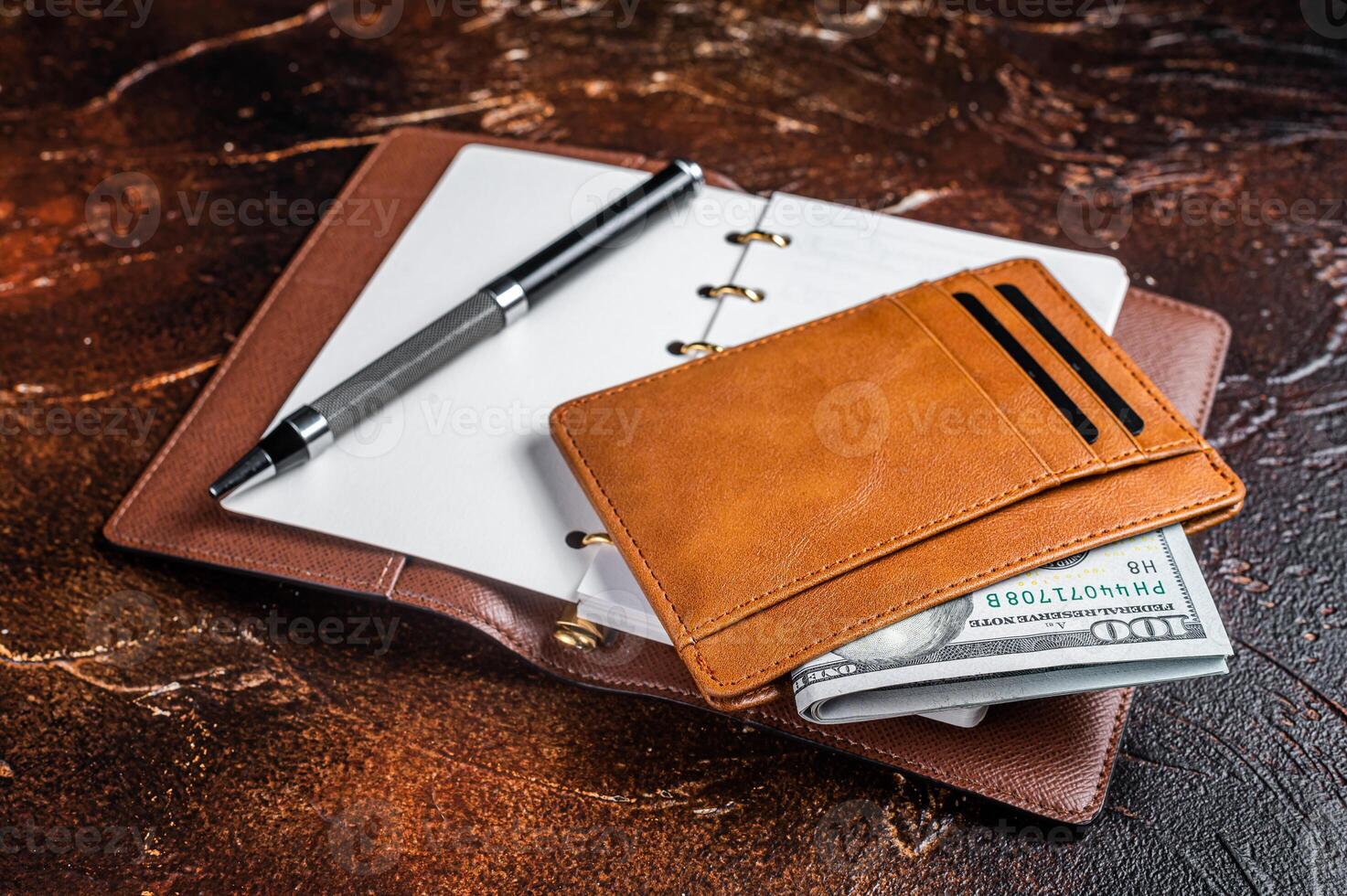 Wooden desk table with blank notebook, pen, wallet with money and credit cards. Brown background. Top view. Copy space photo