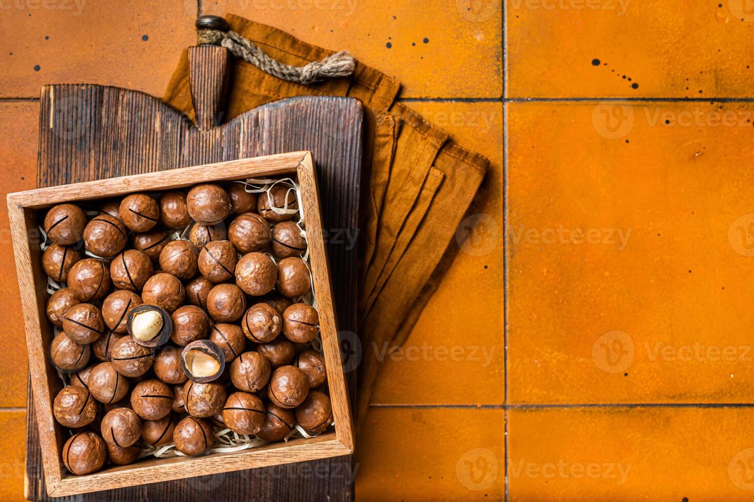 Macadamia natural nuts in a box. Orange background. Top view. Copy space photo