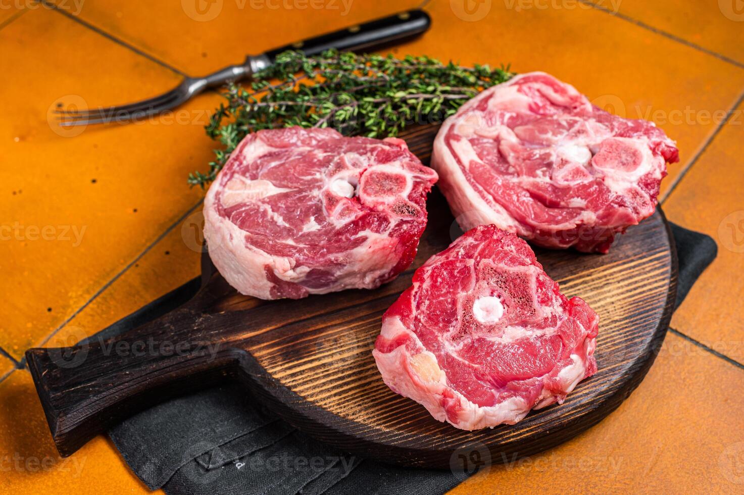 Raw lamb neck chops, fresh mutton meat on a butcher board with herbs. Orange background. Top view photo