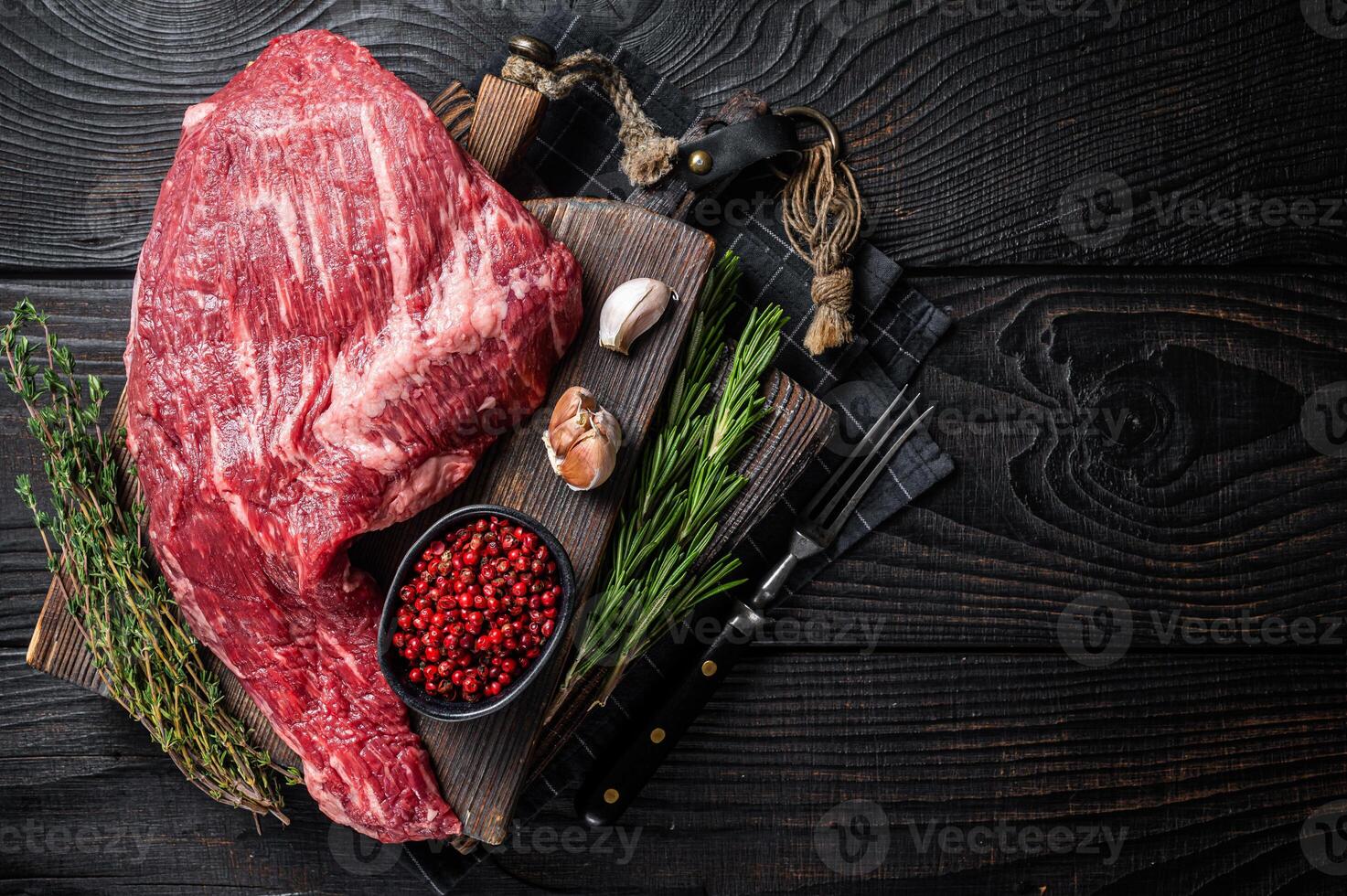 Tri Tip black angus beef steak on cutting board with herbs, raw meat. Black Wooden background. Top view. Copy space photo