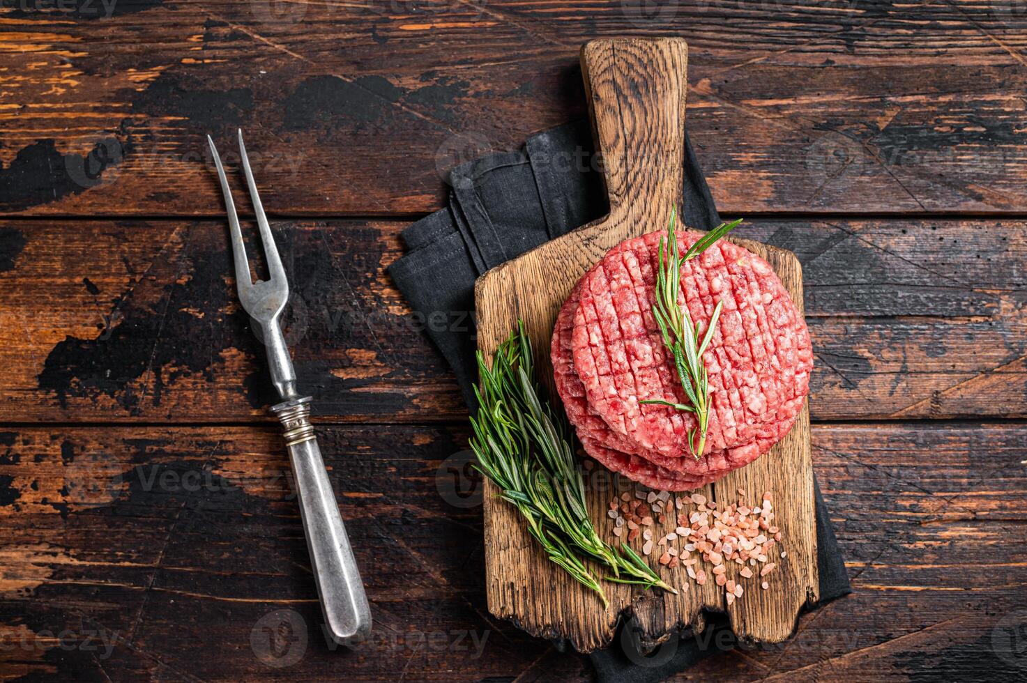 Raw minced homemade farmers grill beef burgers on chopping board with salt and rosemary. Wooden background. Top view photo