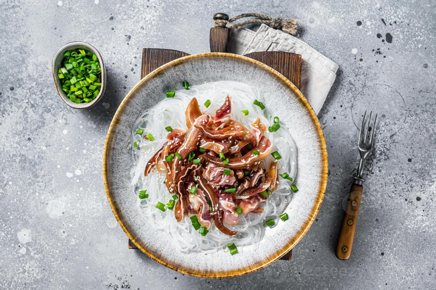 Salad with pork pig ears, glass noodles, sesame seeds and green onions. Fried pork ears in korean style. Gray background. Top view photo