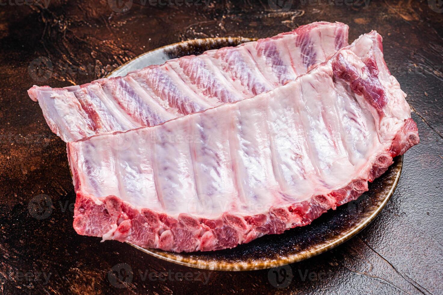Raw Pork Spareribs, uncooked spare ribs on a plate. Dark background. Top view photo