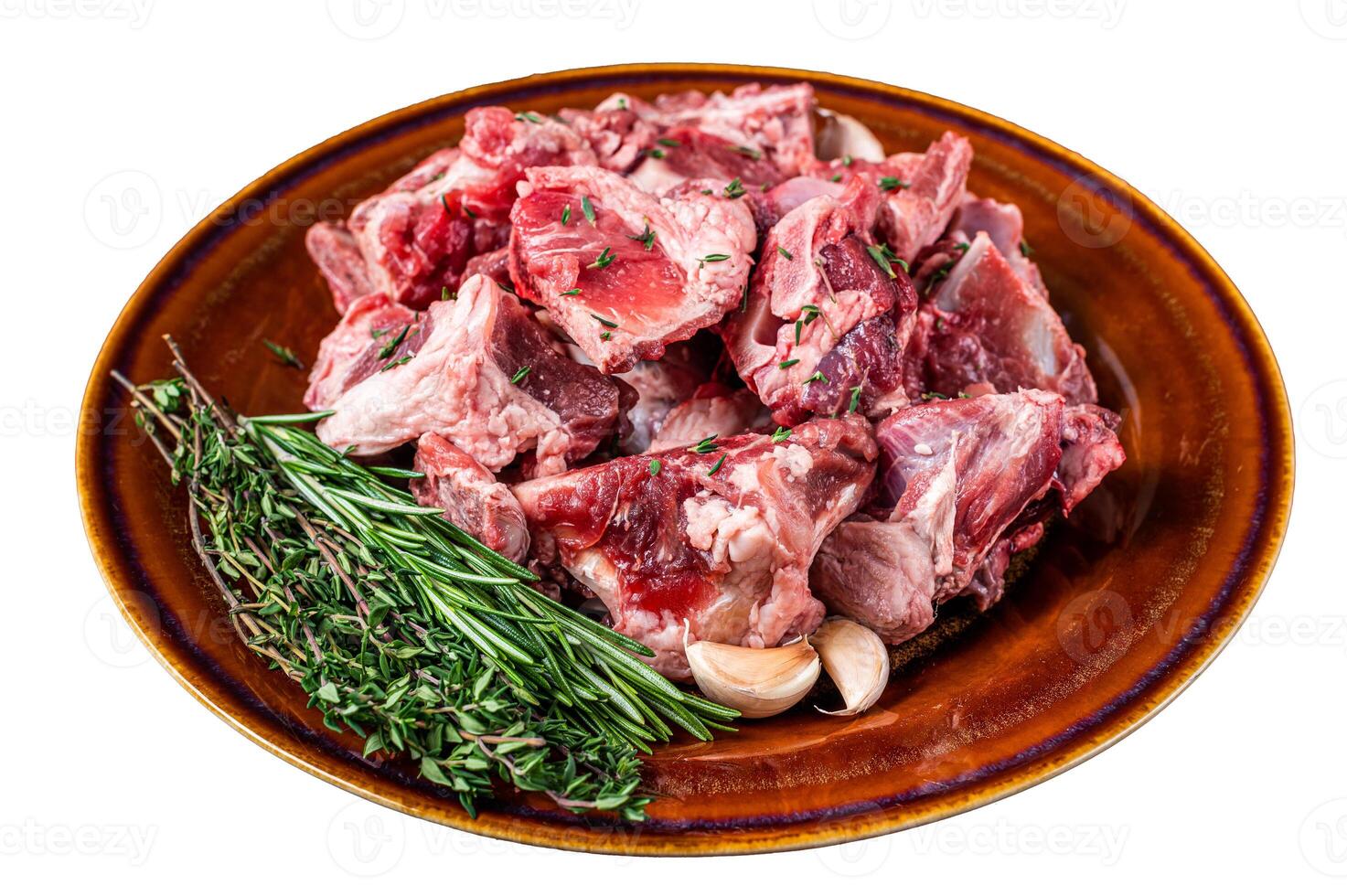 Raw mutton meat diced for goulash or stew with bone on a rustic plate. Isolated on white background. photo