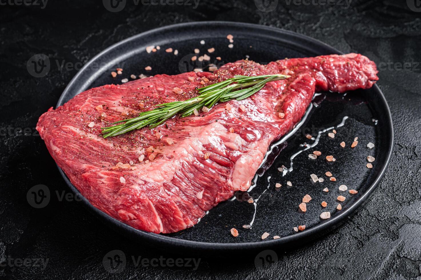 Seasoned raw tri-tip beef meat steak on plate. Black background. Top view photo