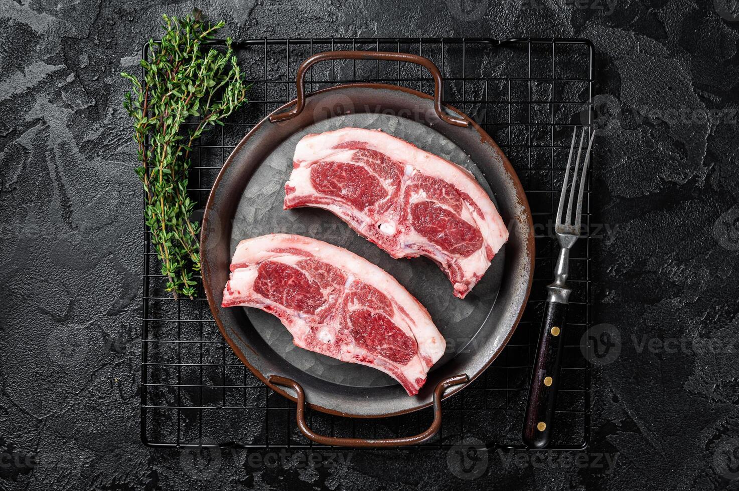 Raw fresh lamb loin chops with herbs and spices in steel tray. Black background. Top view photo