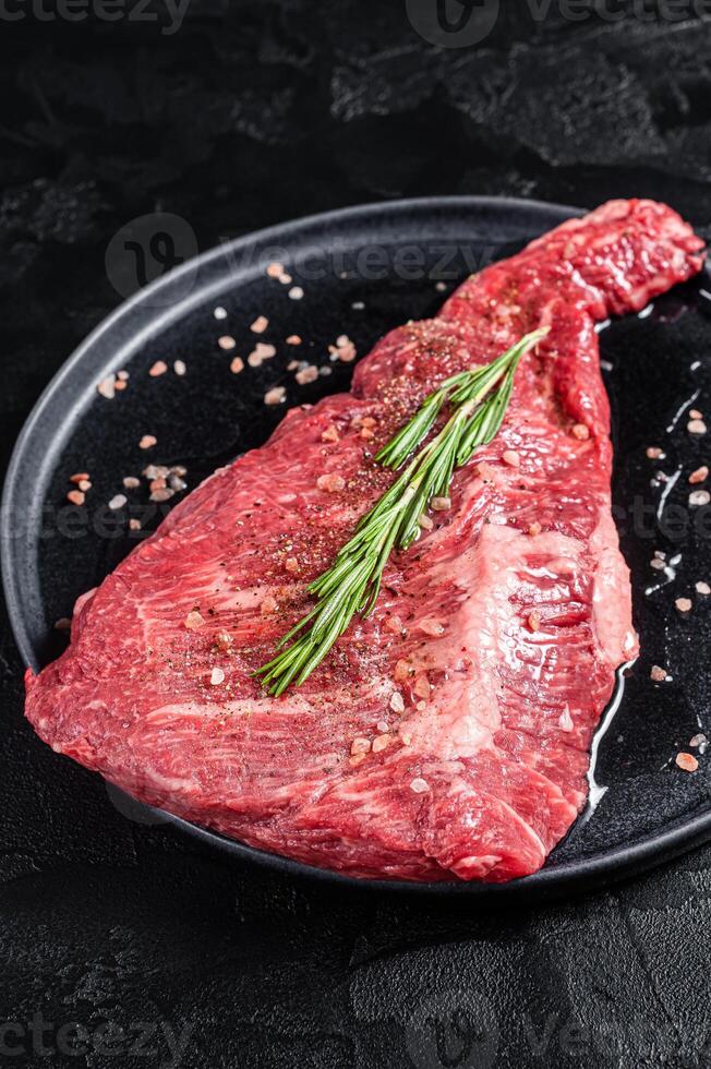 Seasoned raw tri-tip beef meat steak on plate. Black background. Top view photo
