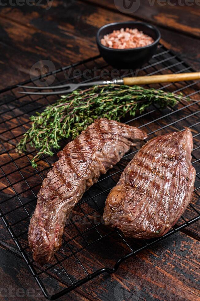 Grilled Sirloin flap or Bavette beef meat steak on a griil with herbs. Wooden background. Top view photo