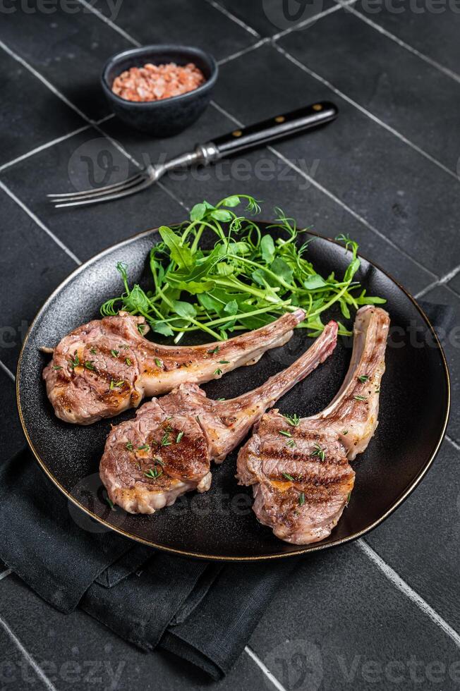 Roasted lamb meat cutlets, mutton chops with garnish. Black background. Top view photo