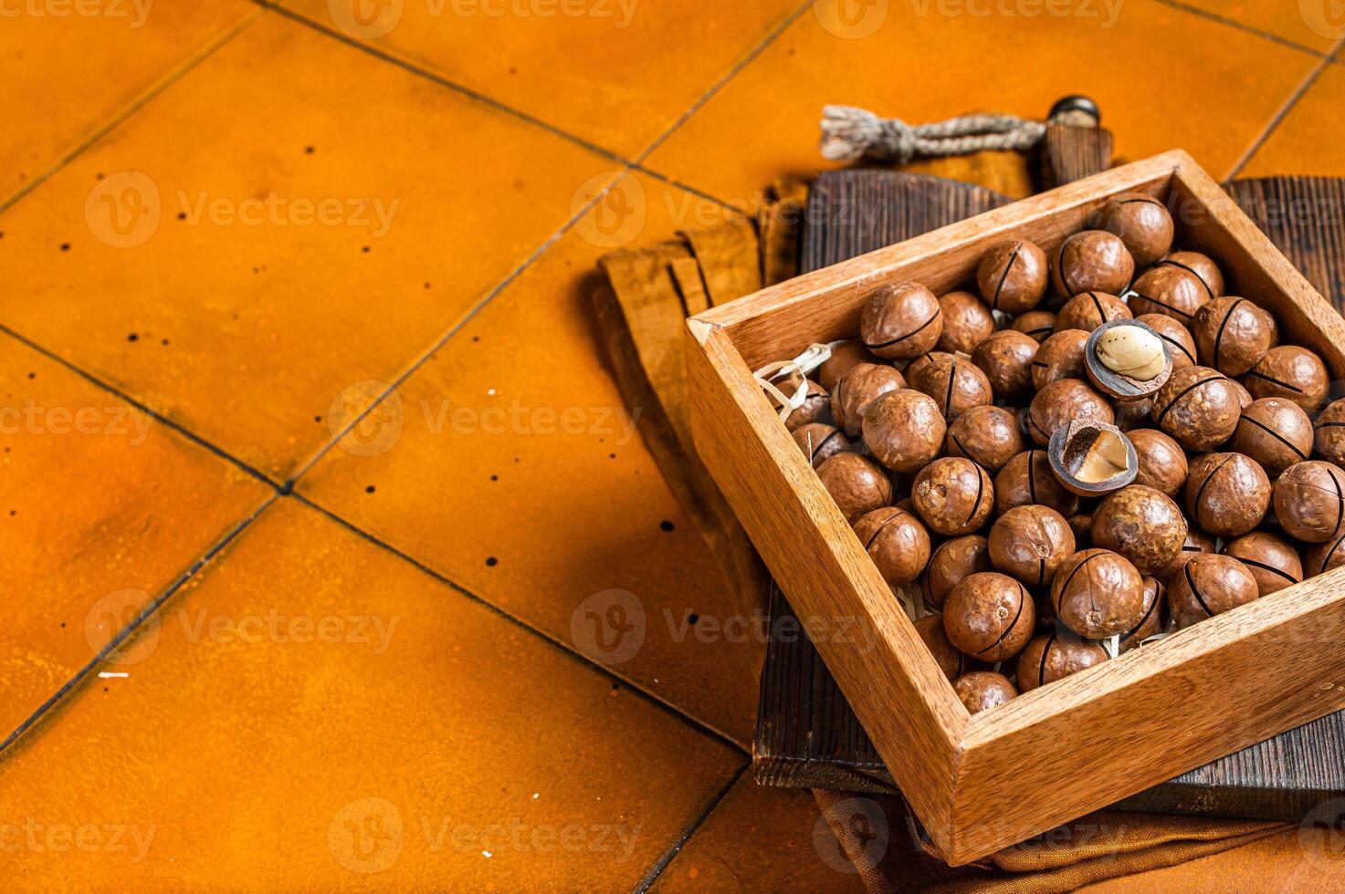 Macadamia natural nuts in a box. Orange background. Top view. Copy space photo