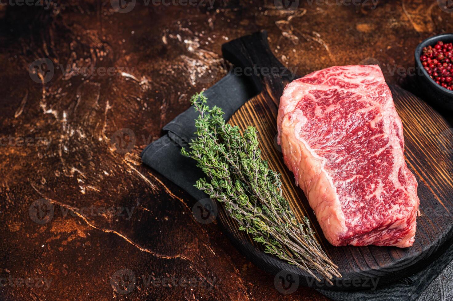 Uncooked Raw striploin or club steak on wooden board with thyme. Dark background. Top view. Copy space photo