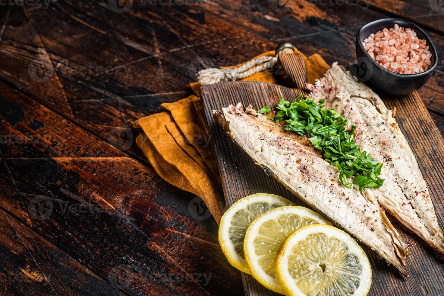Delicious baked mackerel fillets with greens, garlic and lemon on wooden board. Wooden background. Top view. Copy space photo