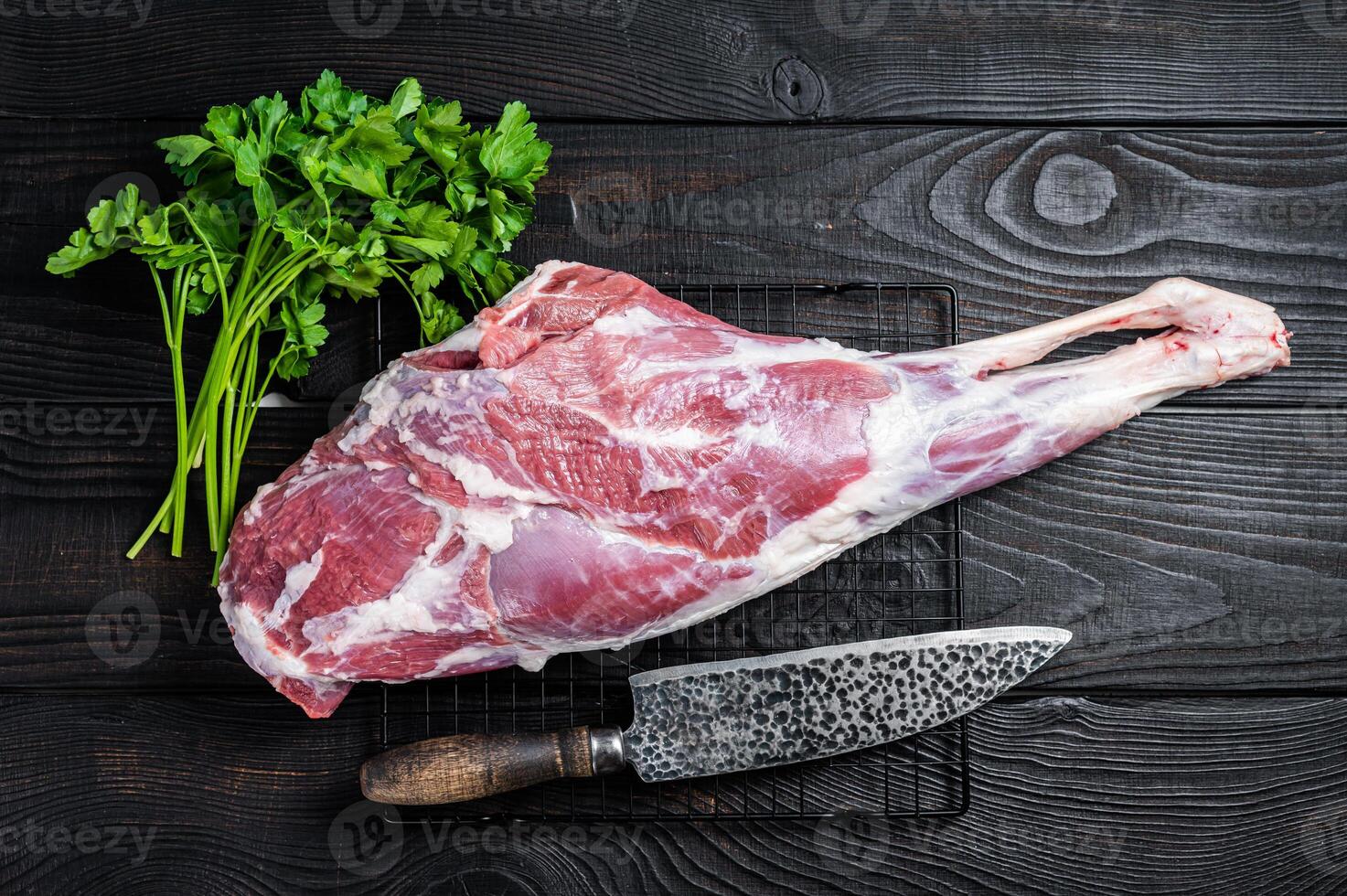 Fresh Raw whole lamb mutton leg thigh on kitchen table with herbs. Black Wooden background. Top view photo