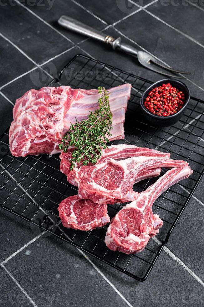 Fresh Raw lamb meat chop steaks on kitchen table with spices and herbs. Black background. Top view photo