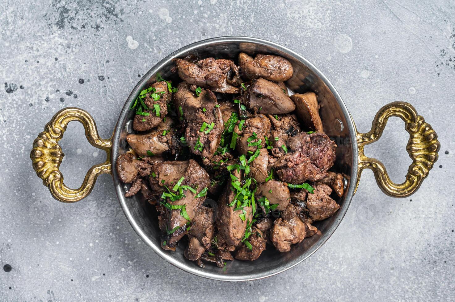 Chicken liver stew with onions and parsley in a skillet. Gray background. Top view photo