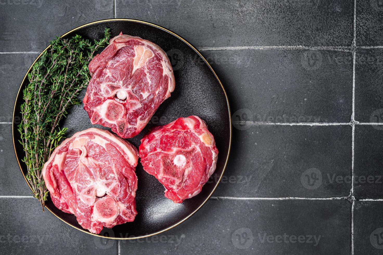 Raw Lamb Gerdan, lamb neck chops on a plate with herbs. Black background. Top view. Copy space photo