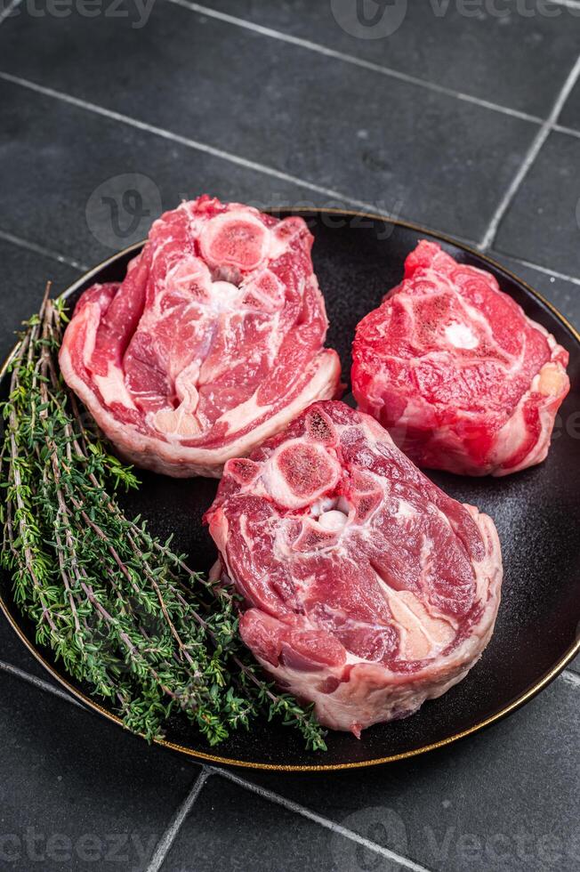Raw Lamb Gerdan, lamb neck chops on a plate with herbs. Black background. Top view photo