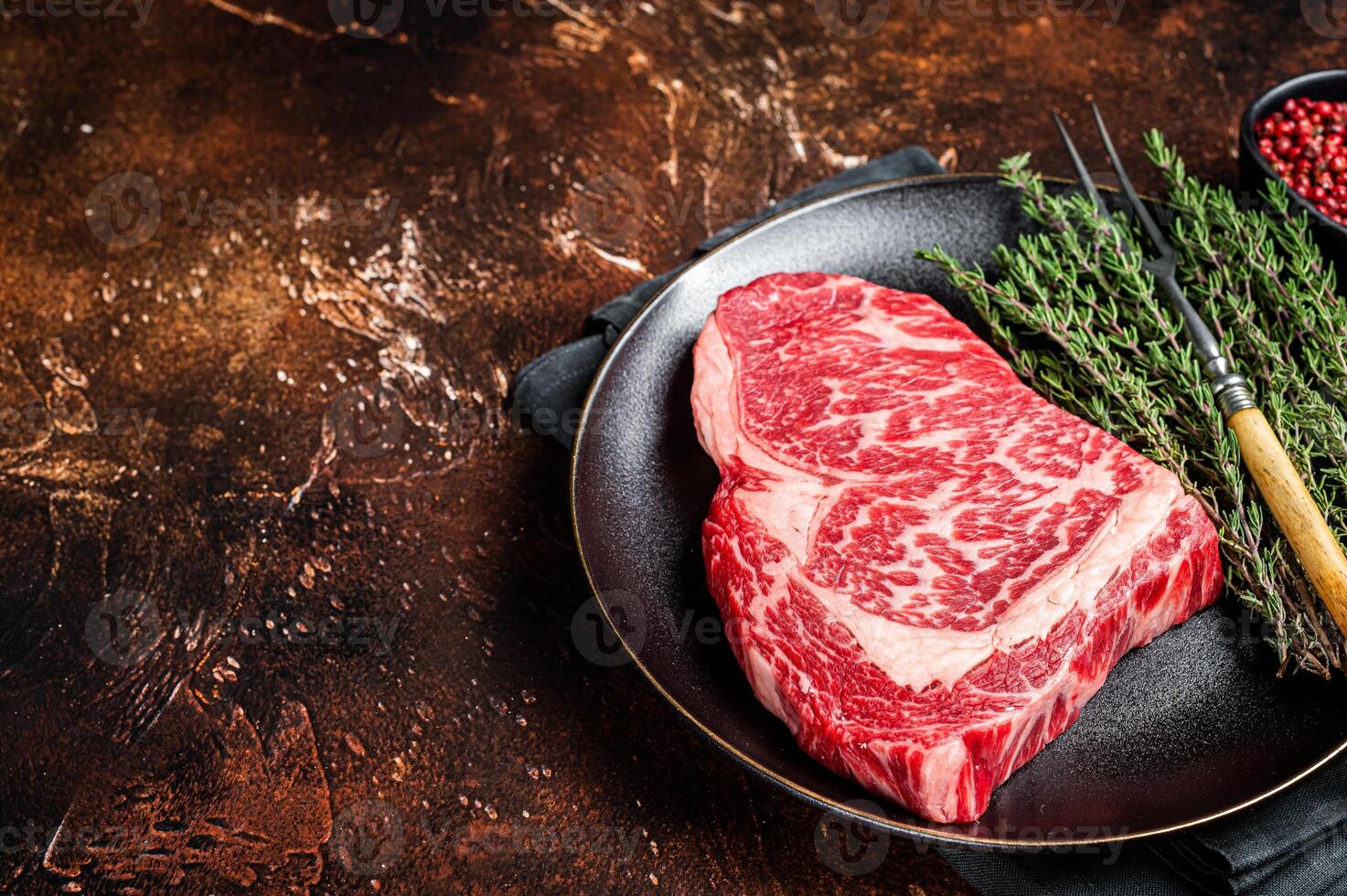 Black Angus Rib Eye steak, raw marbled beef meat with herbs. Dark background. Top view. Copy space photo