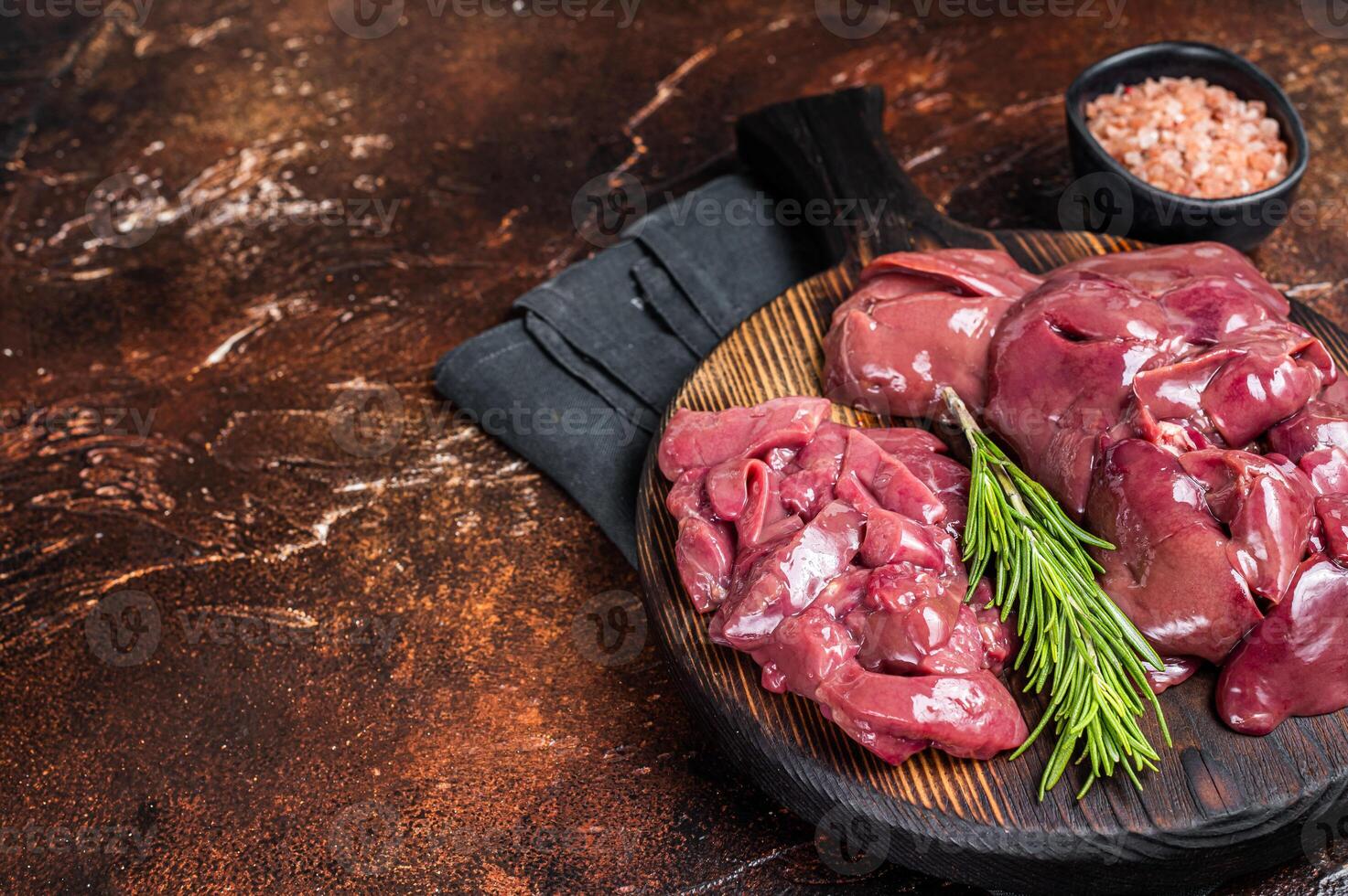 Sliced Raw chicken liver, fresh fowl offals on wooden board. Dark background. Top view. Copy space photo