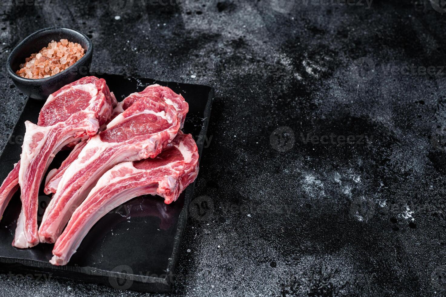 Uncooked lamb mutton chops, raw meat steaks. Black background. Top view. Copy space photo