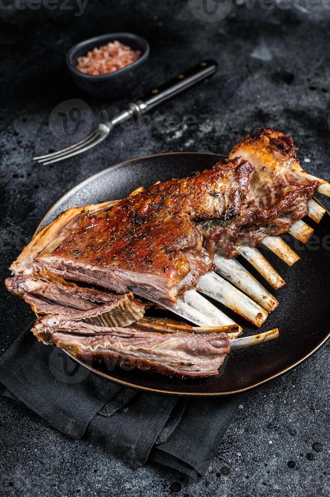 Roasted Rack of lamb ribs, mutton spareribs, sliced meat on plate. Black background. Top view photo