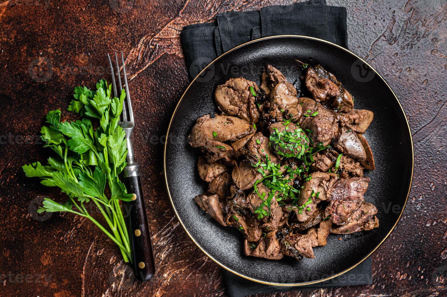 Fried chicken liver with onions and parsley in a plate. Dark background. Top view photo