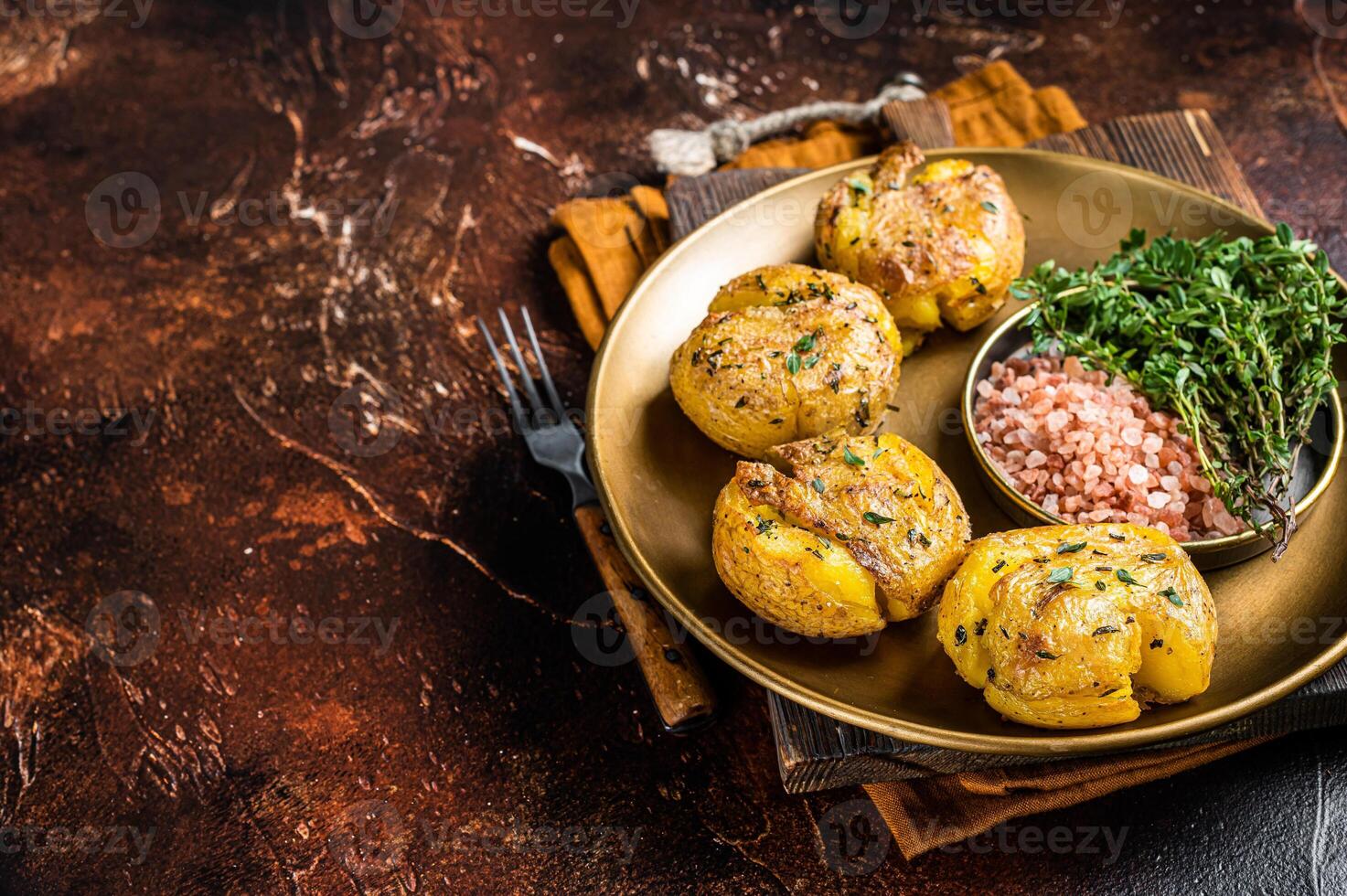 Crushed, smashed potatoes baked with rosemary and thyme on plate. Dark background. Top view. Copy space photo
