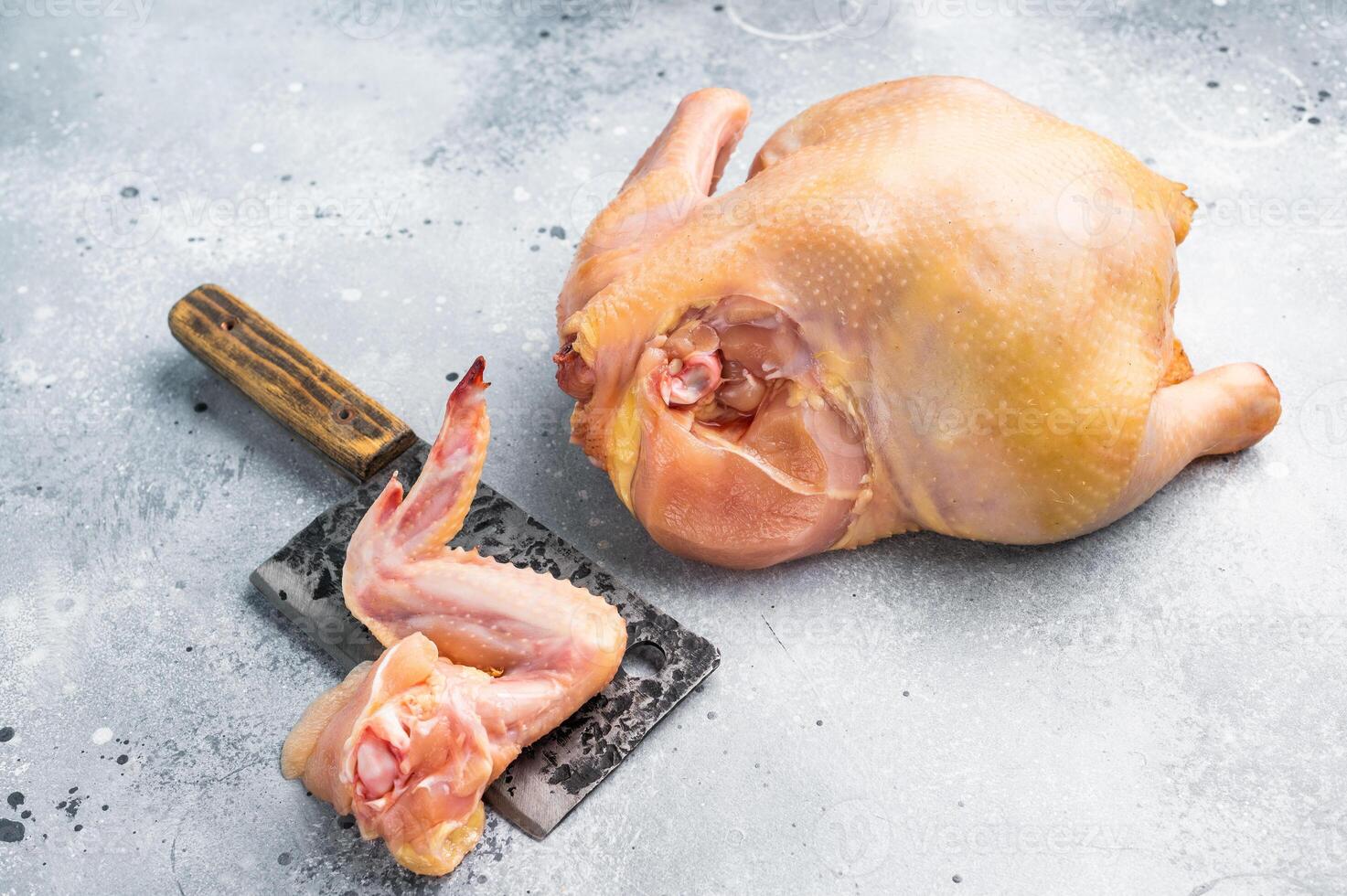 A raw chicken wing sits on a cutting board next to a whole chicken on a gray surface photo