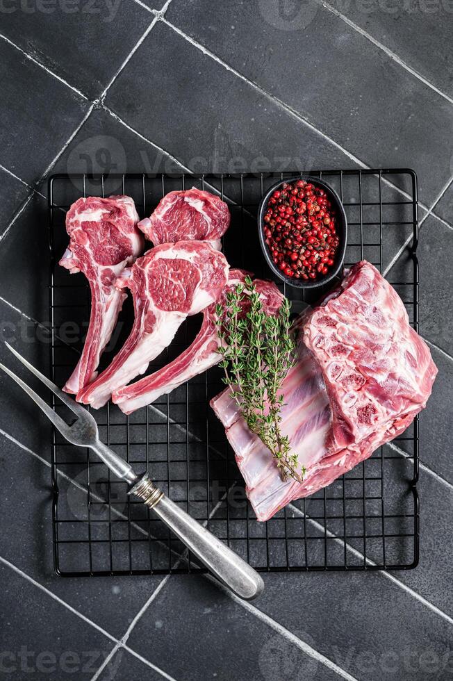Fresh Raw lamb meat chop steaks on kitchen table with spices and herbs. Black background. Top view photo