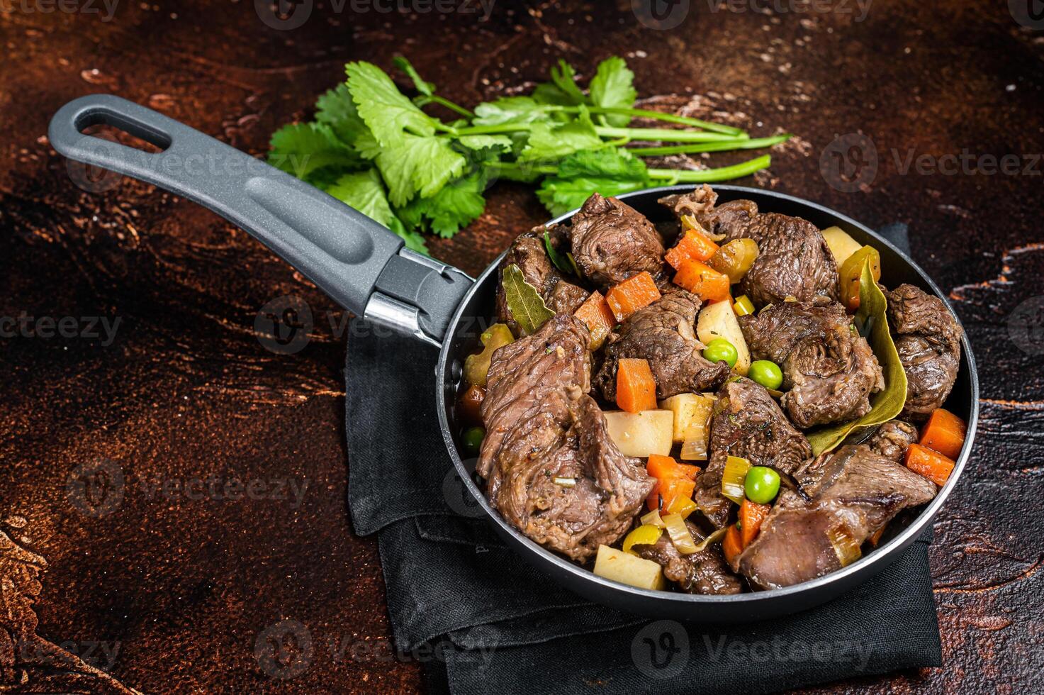 Irish stew with beef meat, potatoes, carrots and herbs in a skillet. Dark background. Top view photo
