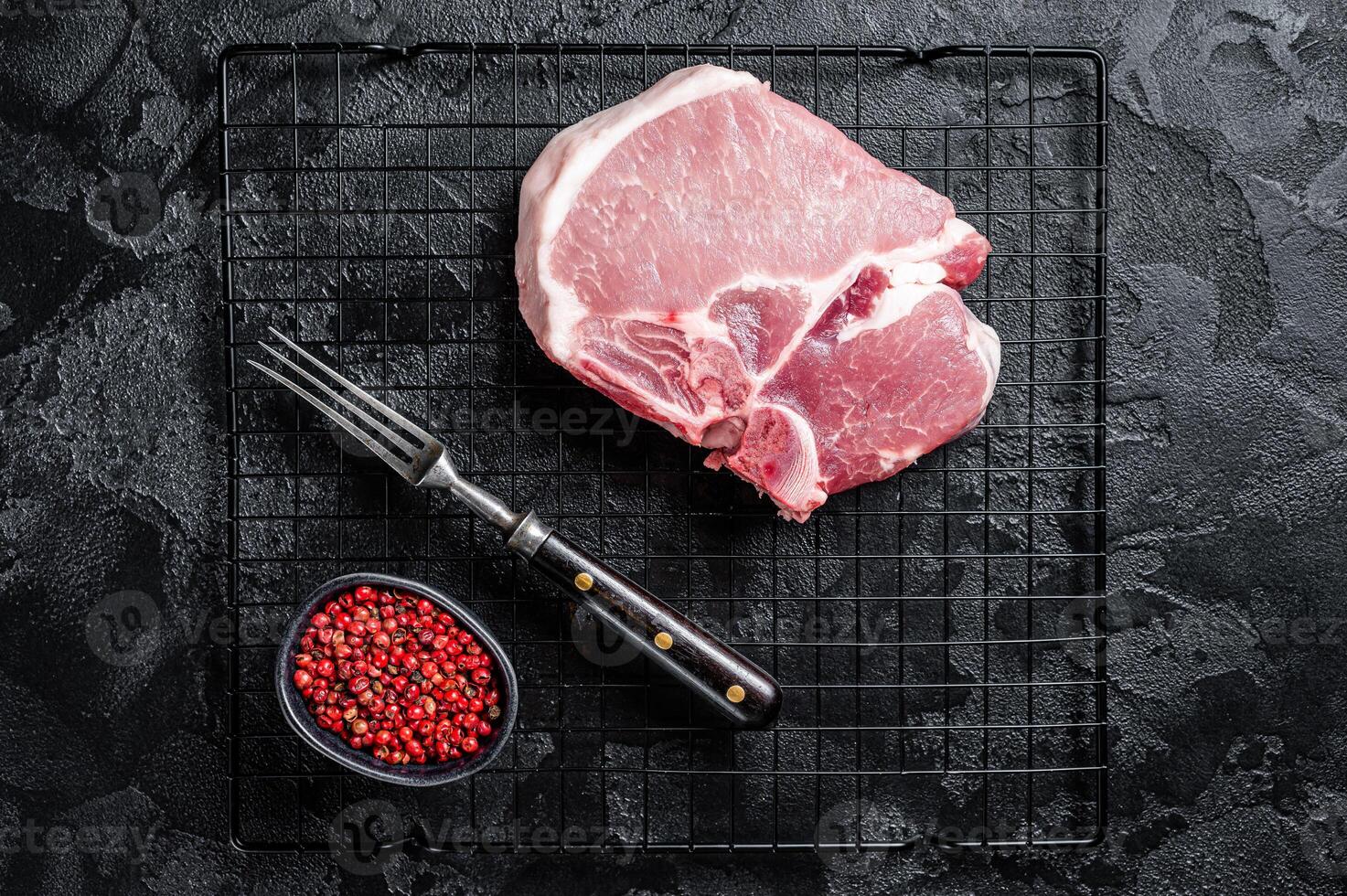 Uncooked Raw pork T bone chop meat steak on grill. Black background. Top view photo