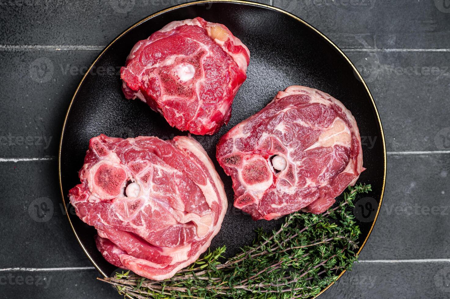 Raw Lamb Gerdan, lamb neck chops on a plate with herbs. Black background. Top view photo