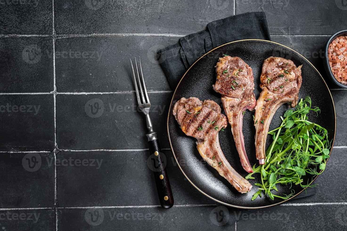 Roasted lamb meat cutlets, mutton chops with garnish. Black background. Top view. Copy space photo