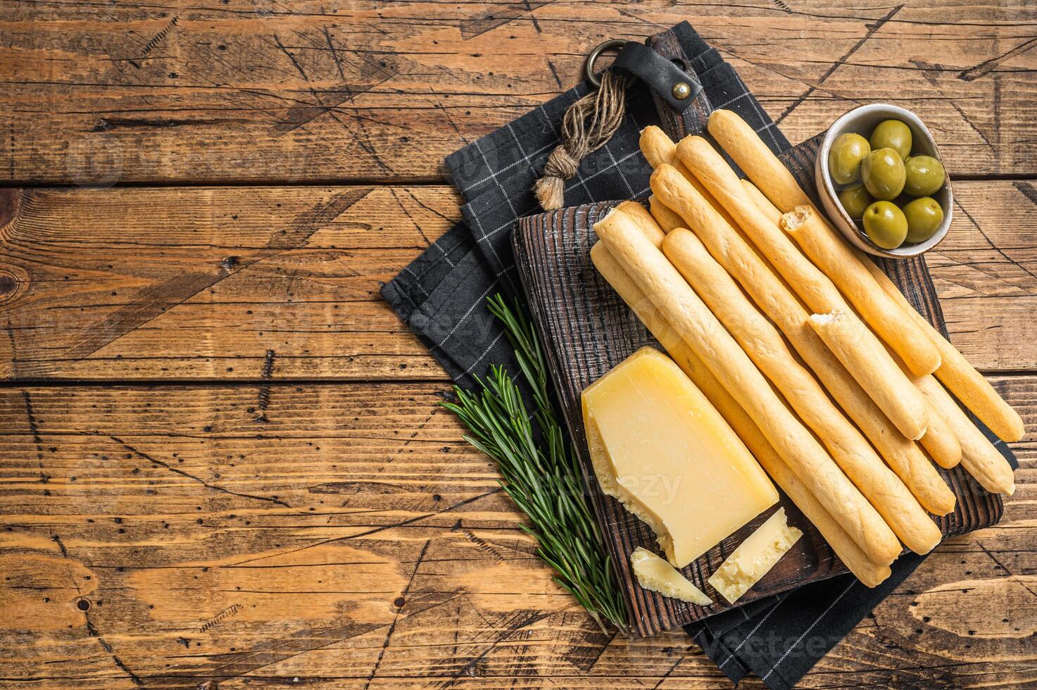 Traditional italian appetizer grissini bread sticks on wooden board with olives and parmesan cheese. Wooden bakground. Top view. Copy space photo