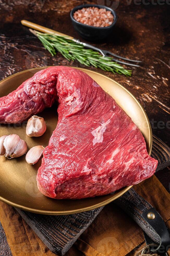 Raw tri-tip triangle roast or bottom sirloin steak on plate with herbs. Dark background. Top view photo